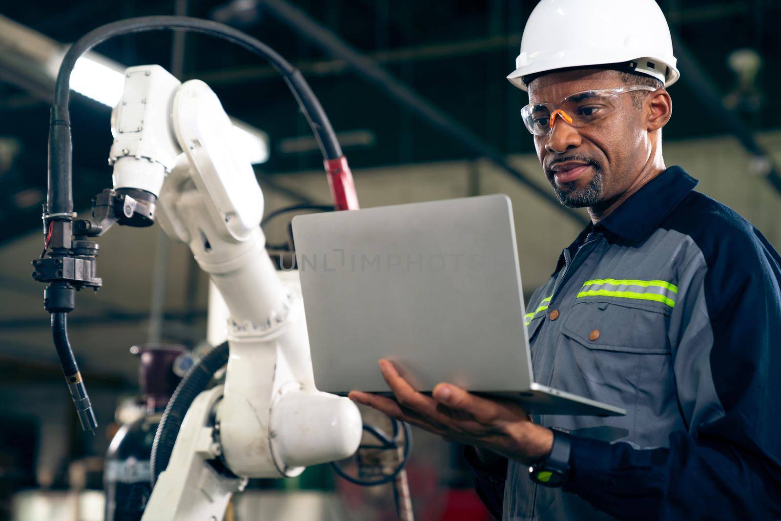 African American factory worker working with adept robotic arm by biancoblue