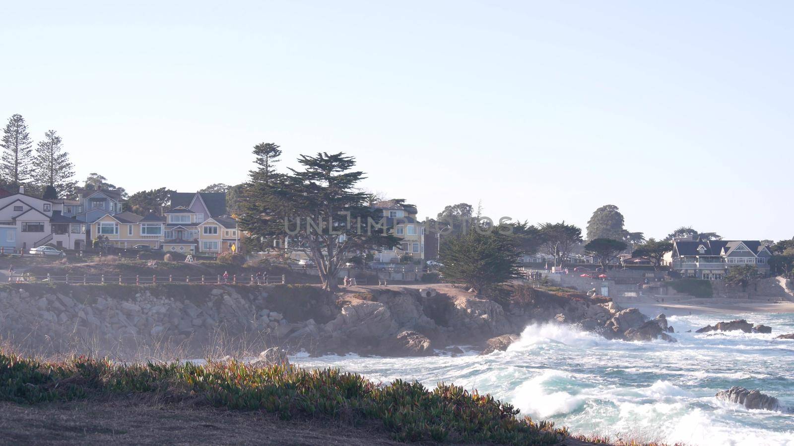 Rocky craggy ocean beach, sea waves crashing on shore, Monterey 17-mile drive, California coast, USA. Pacific Grove, beachfront waterfront promenade, waterside historic houses, colonial architecture.