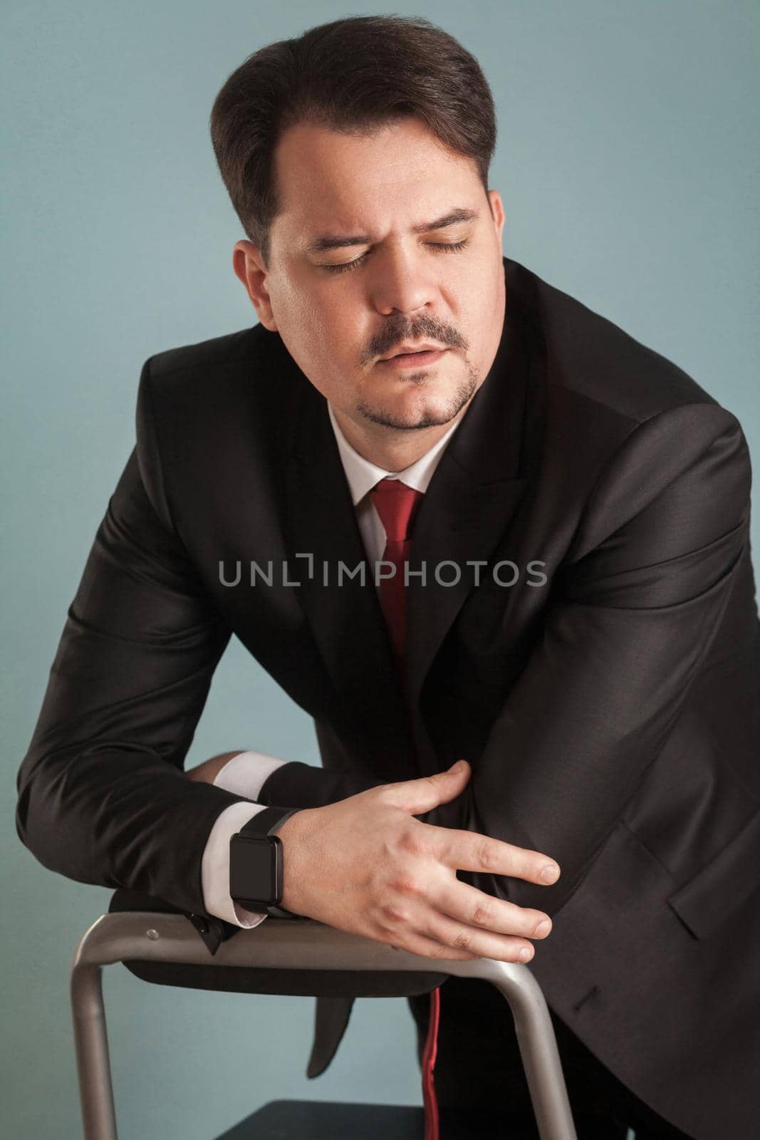 Portrait of business man, closed eyes and have unhappy look. Indoor, studio shot, isolated on light blue or gray background