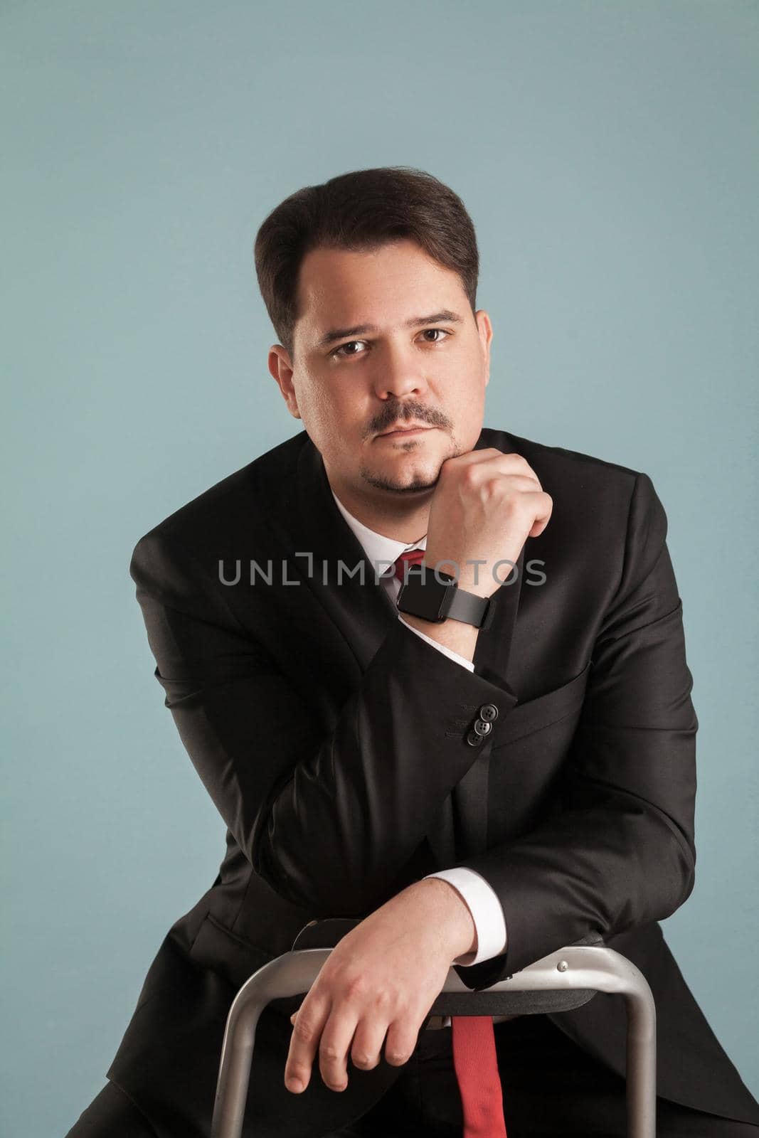 Portrait of acting shoot sitting businessman touching chin, looking at camera by Khosro1