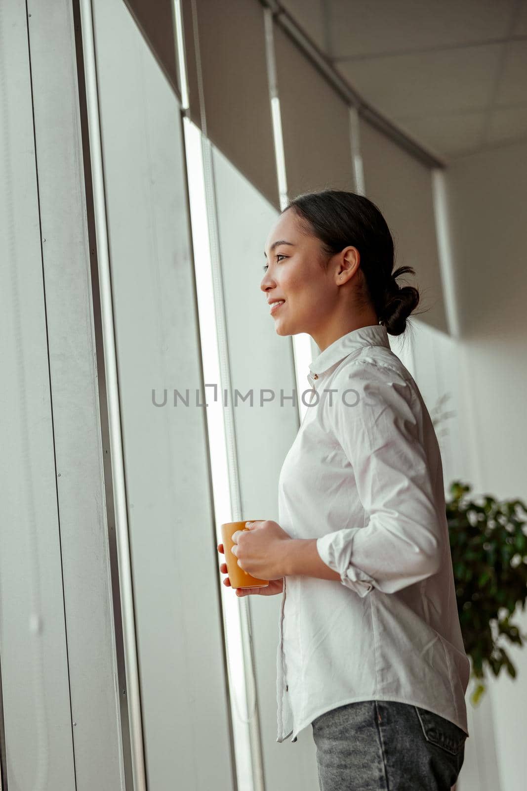 Charming asian business woman drinking coffee standing near windows at office. High quality photo