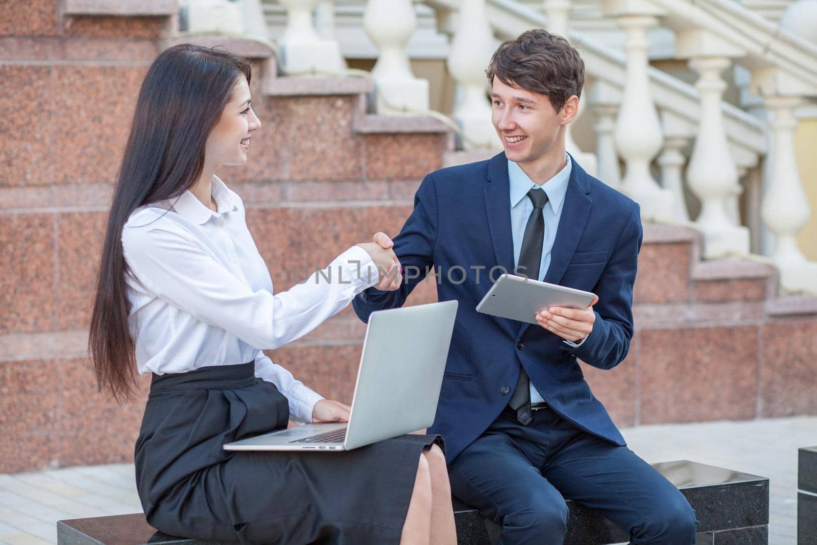 Boss in blue suit and his assistant in white blouse and black skirt discussing their work outdoors.