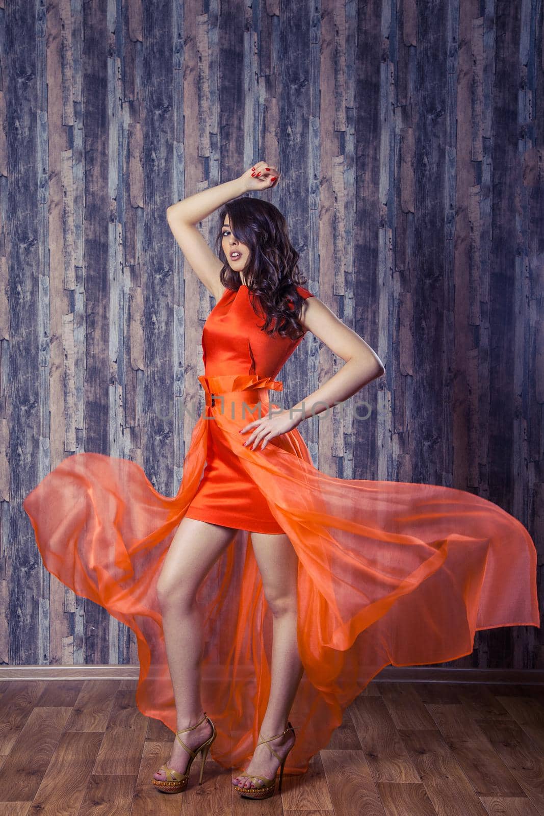 Young brunette woman in stylish orange silk dress posing on wooden background by Khosro1