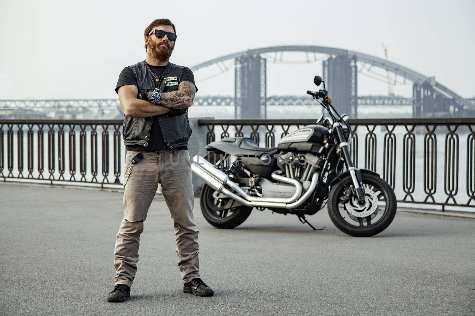 bearded motorcyclist man with his motorbike on summertime posing.