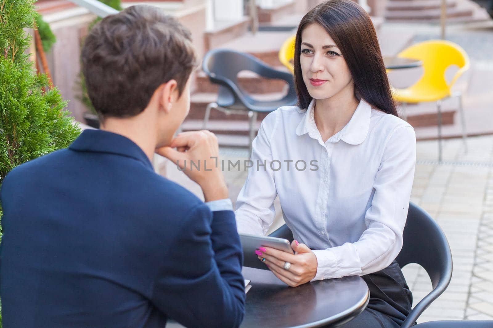 Two friends sitting outdoor in cafe thinking, looking at tablet and discussing their business.