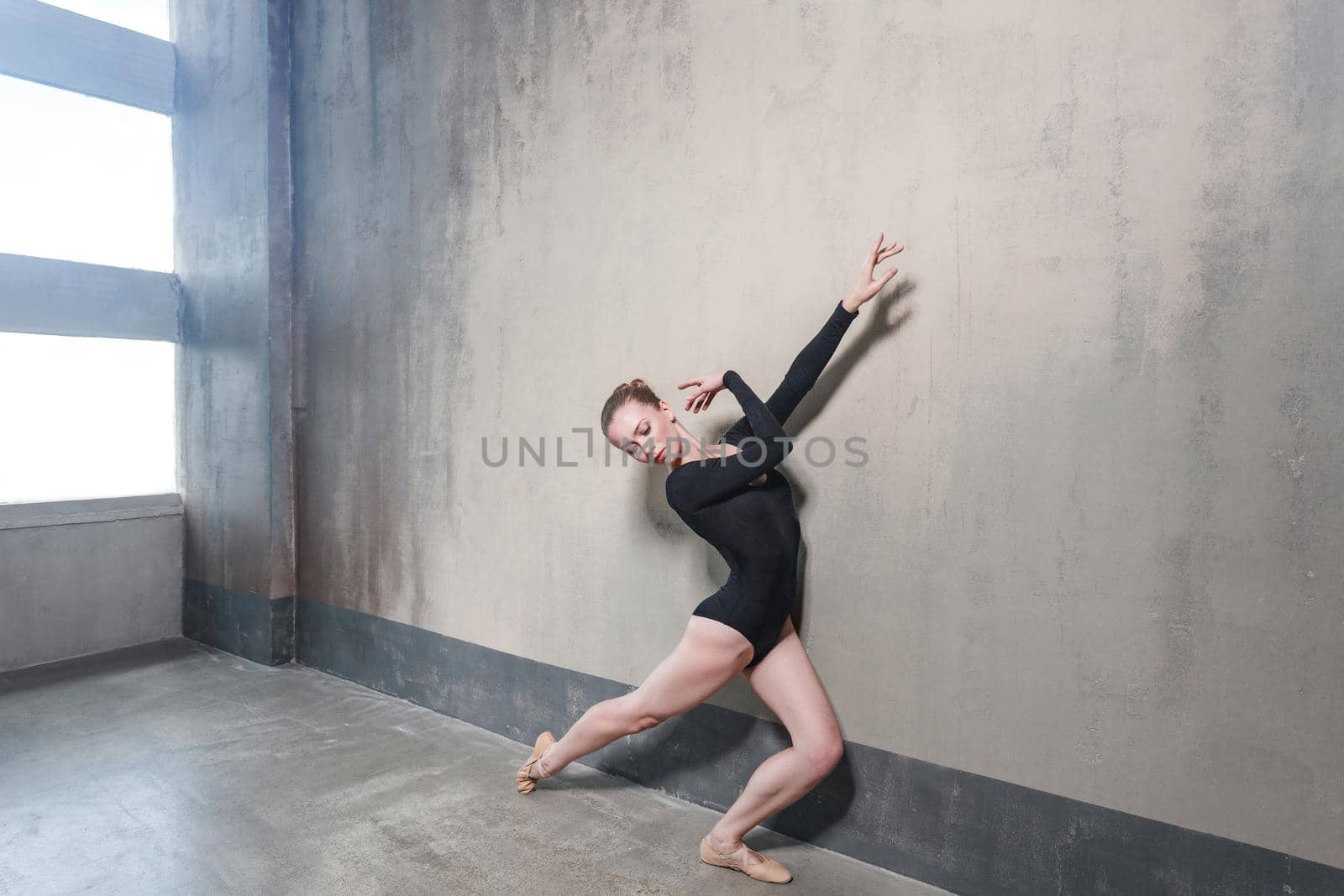 Ballerina movement in classic ballet posing near window. Studio shot, gray wall