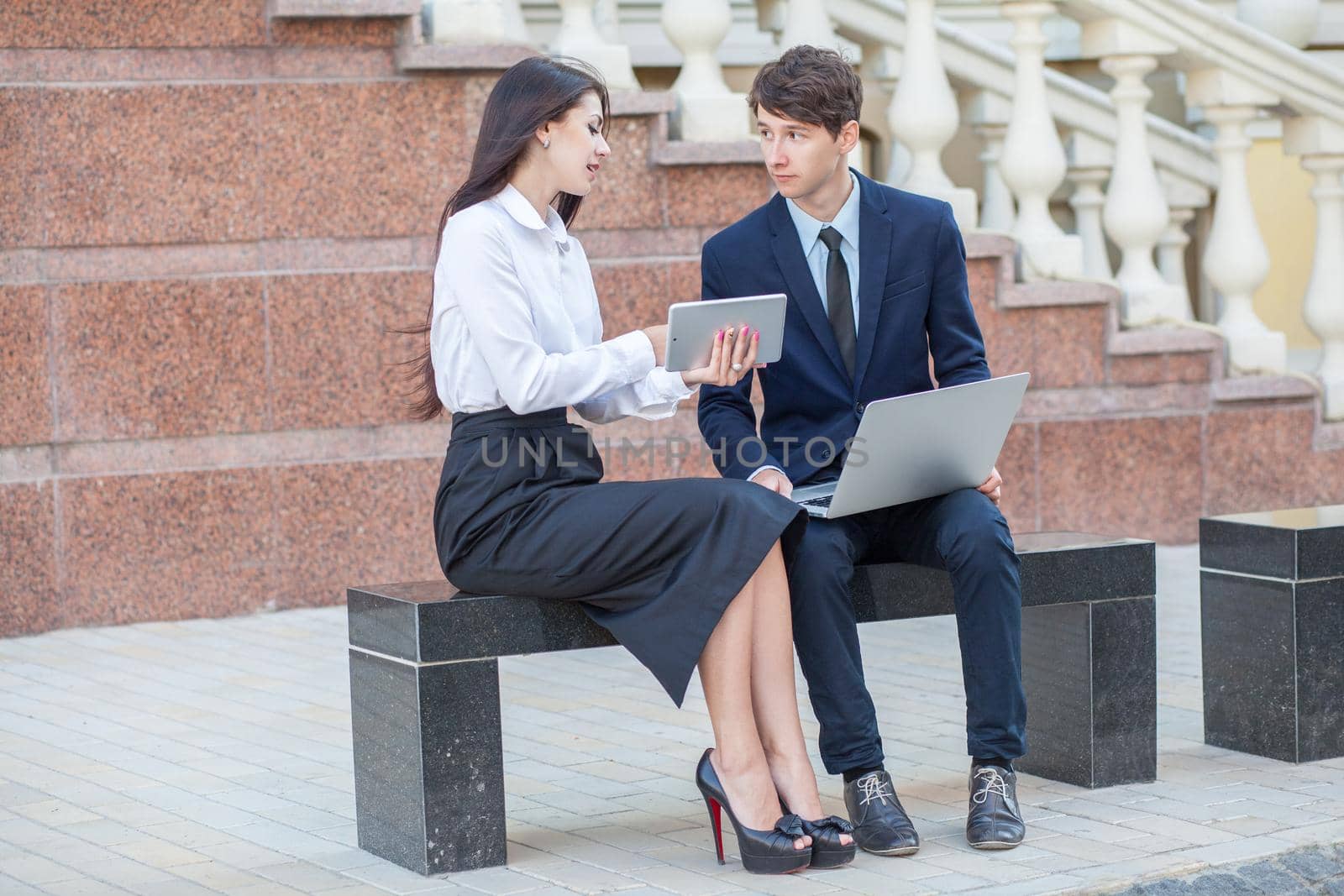 Boss in blue suit and his assistant in white blouse and black skirt discussing their work outdoors.