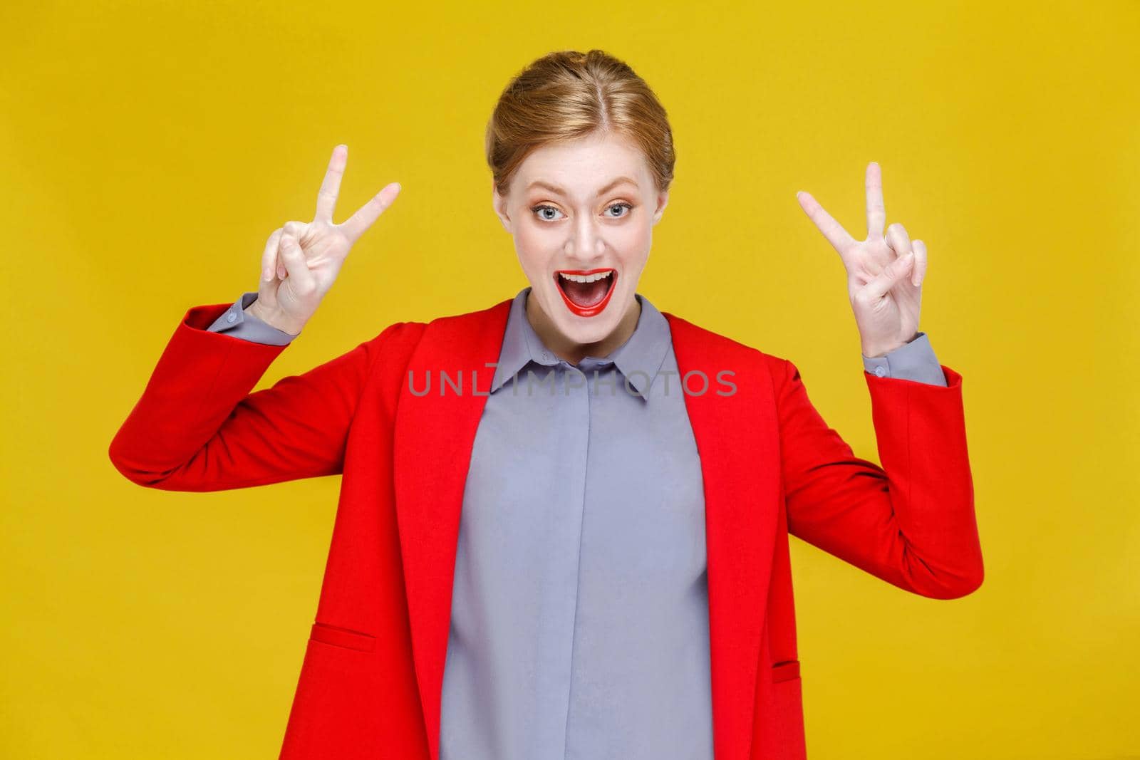 Red head business woman in red suit showing v sign, peace,four sign. Studio shot, isolated on yellow background