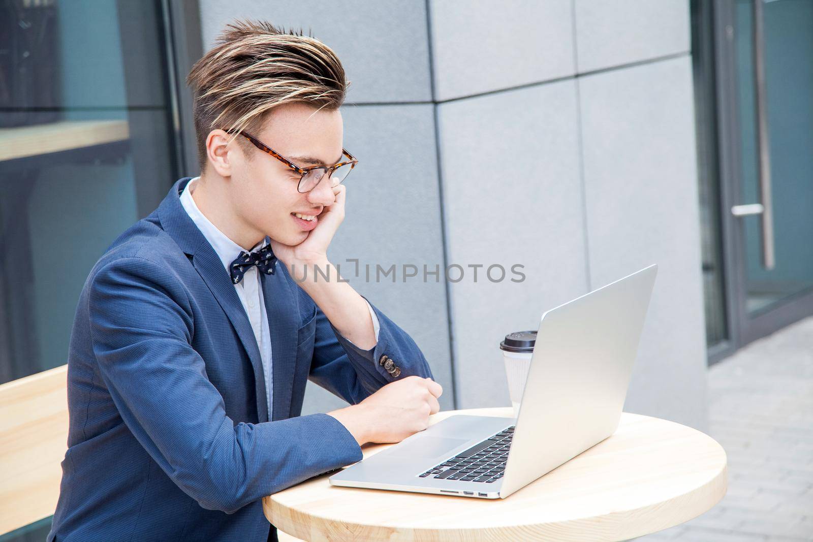 Attractive young freelancer with blue casual suit with laptop and coffee sitting and working. looking at display and smilling.