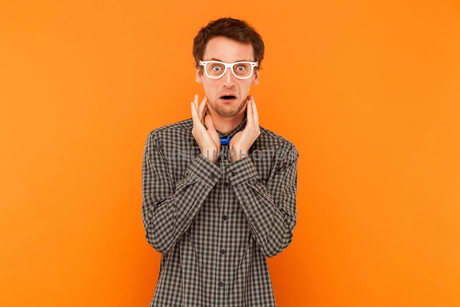 Crazy student looking at camera with shocked face. Indoor, orange background
