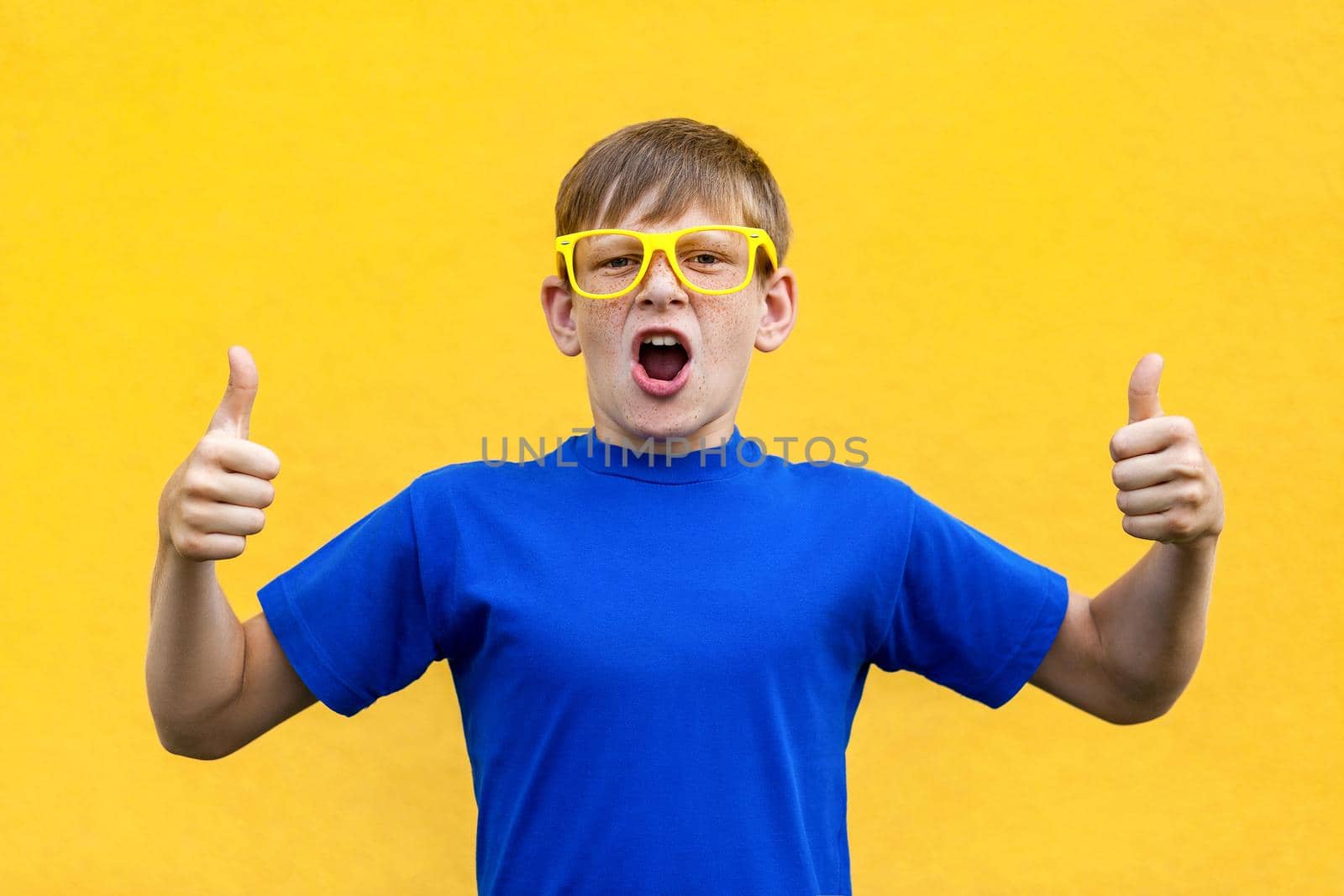 Happiness thumbs up, looking at camera and toothy smile. Studio shot, yellow background