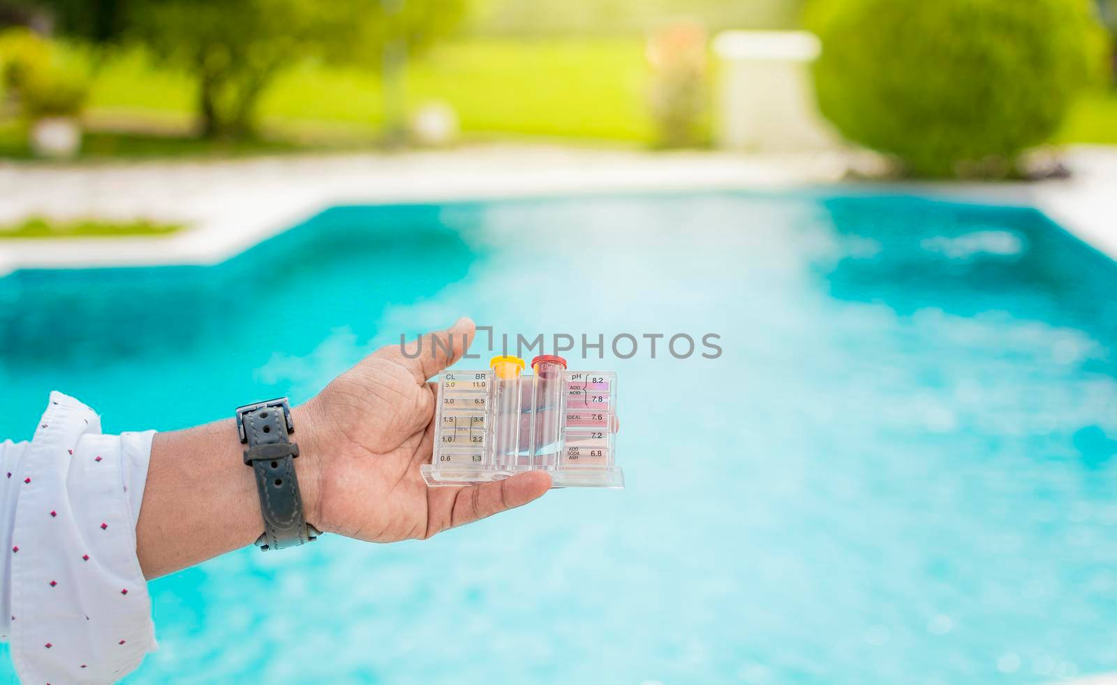 Hand holding Water Test Kit on blurred pool background, Hand holding a pool ph and chlorine tester, Person holding complete water test kit with blurred pool background
