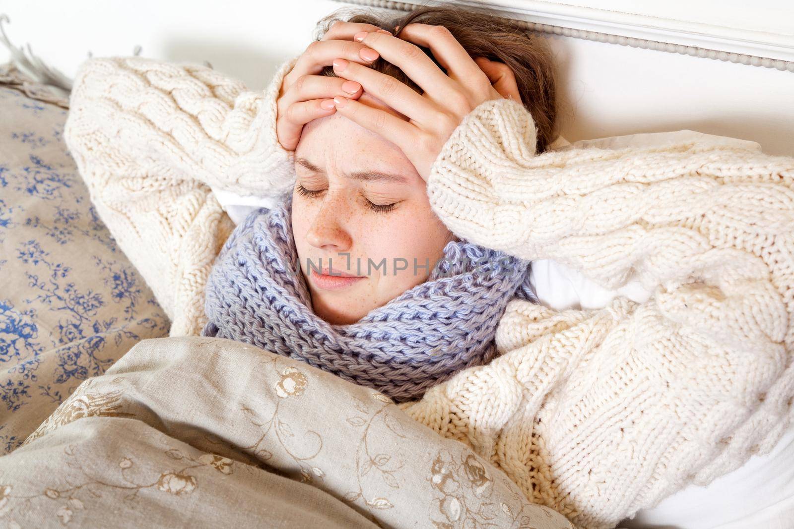 Flu or cold. Closeup top view image of frustrated young woman with blue scarf and suffering from terrible headache while lying in bed.
