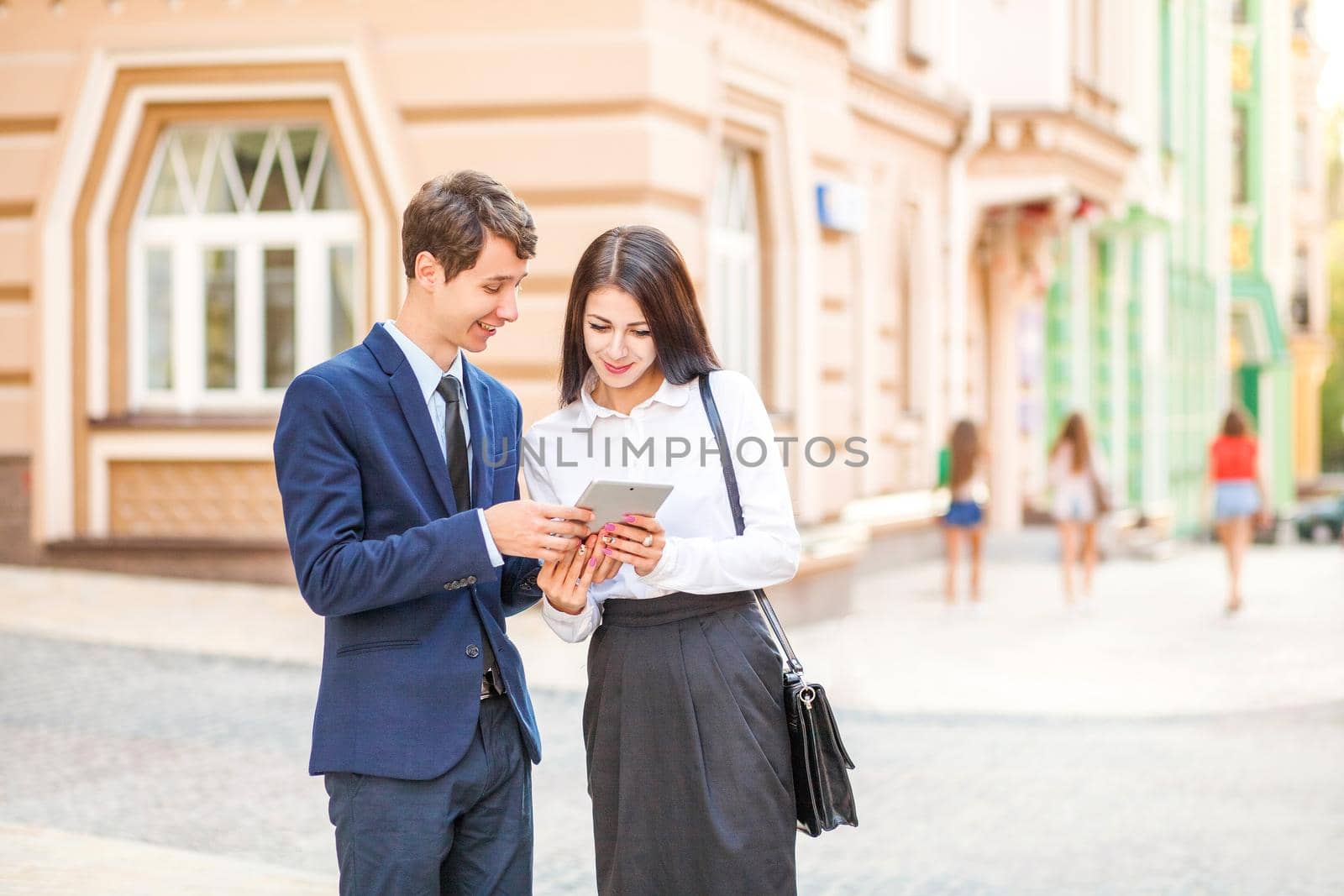 Beautiful young business woman and handsome businessman in formal suits are using a digital tablet in city background. by Khosro1