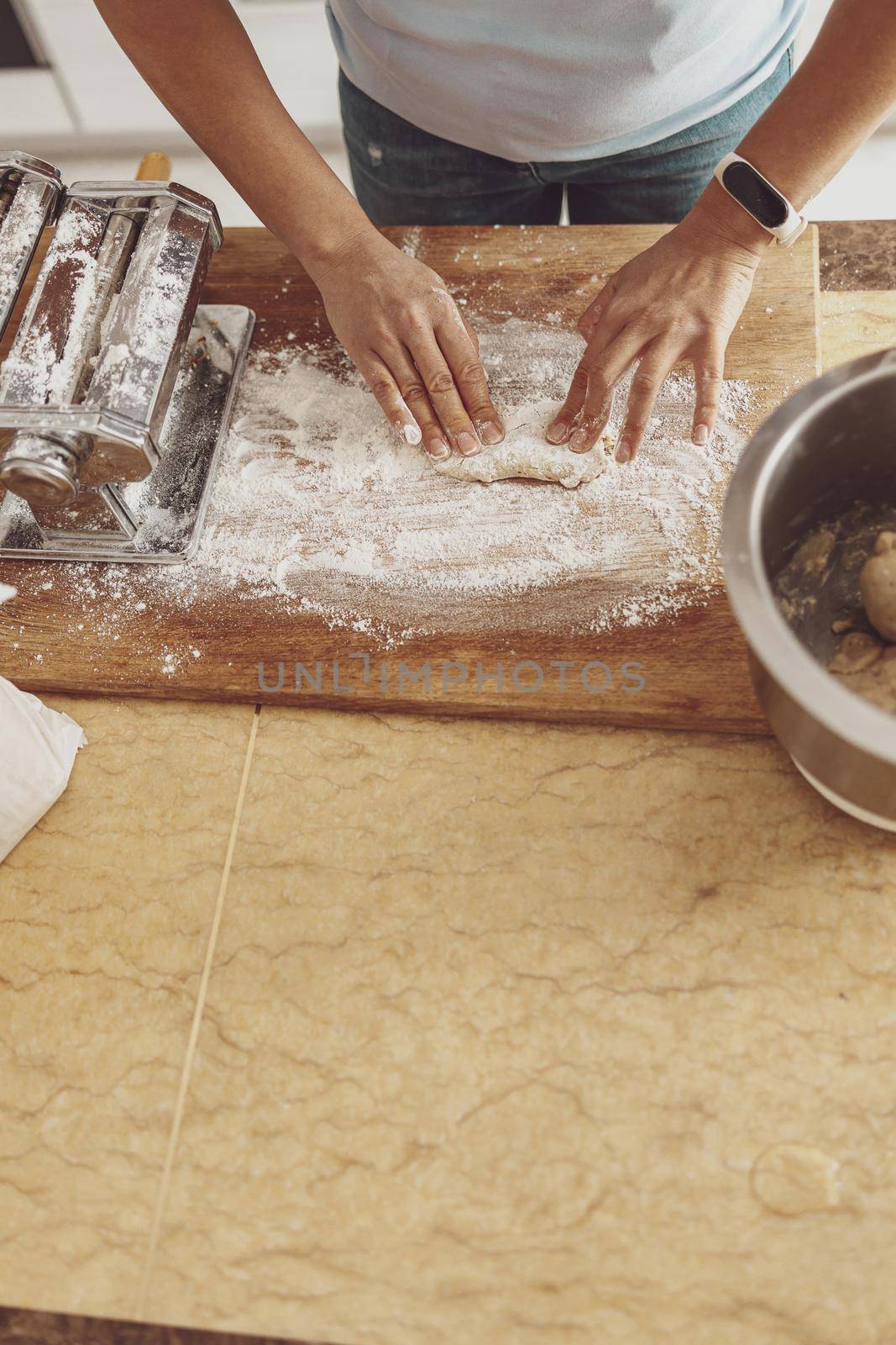 A woman's hands roll out a piece of noodle dough on a wooden board covered with flour. by Yaroslav_astakhov