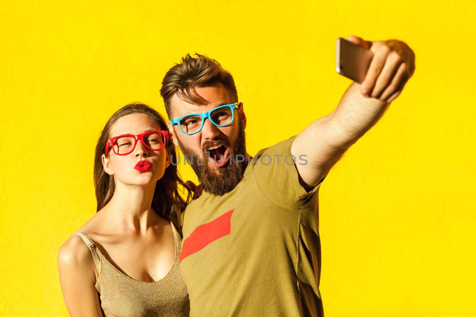Crazy selfie. Beautiful friends macking selfie on yellow background. Studio shot