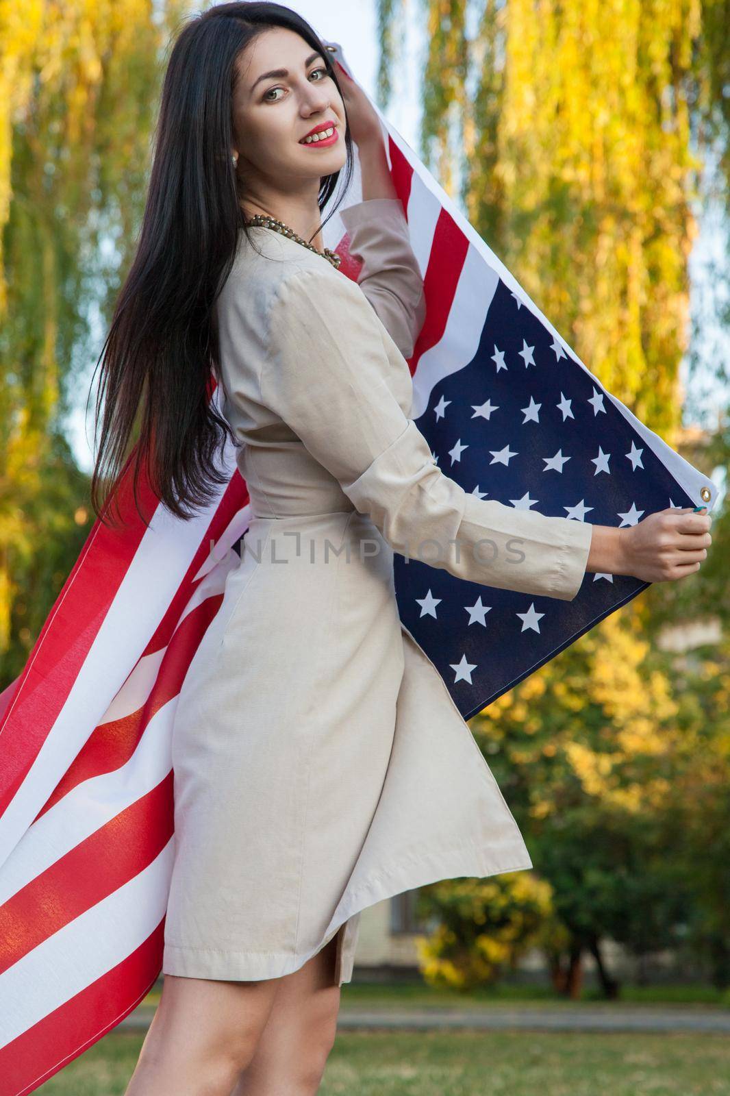 Beautiful young woman with classic dress holding american flag in the park. fashion model holding us smiling and looking at camera. usa lifestyle. by Khosro1