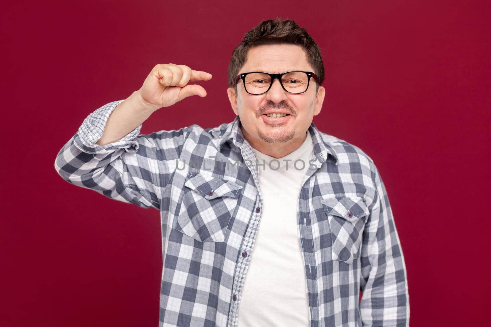 I need a few more. Portrait of hopeful handsome middle aged man in checkered shirt, eyeglasses standing, looking at camera and asking for something more. studio shot, isolated on dark red background.
