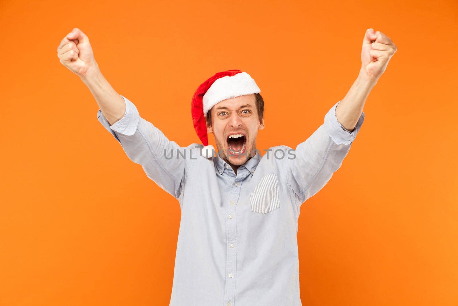 Excited man hands up, shout and looking at camera with big eyes and open mouth. Studio shot, orange background