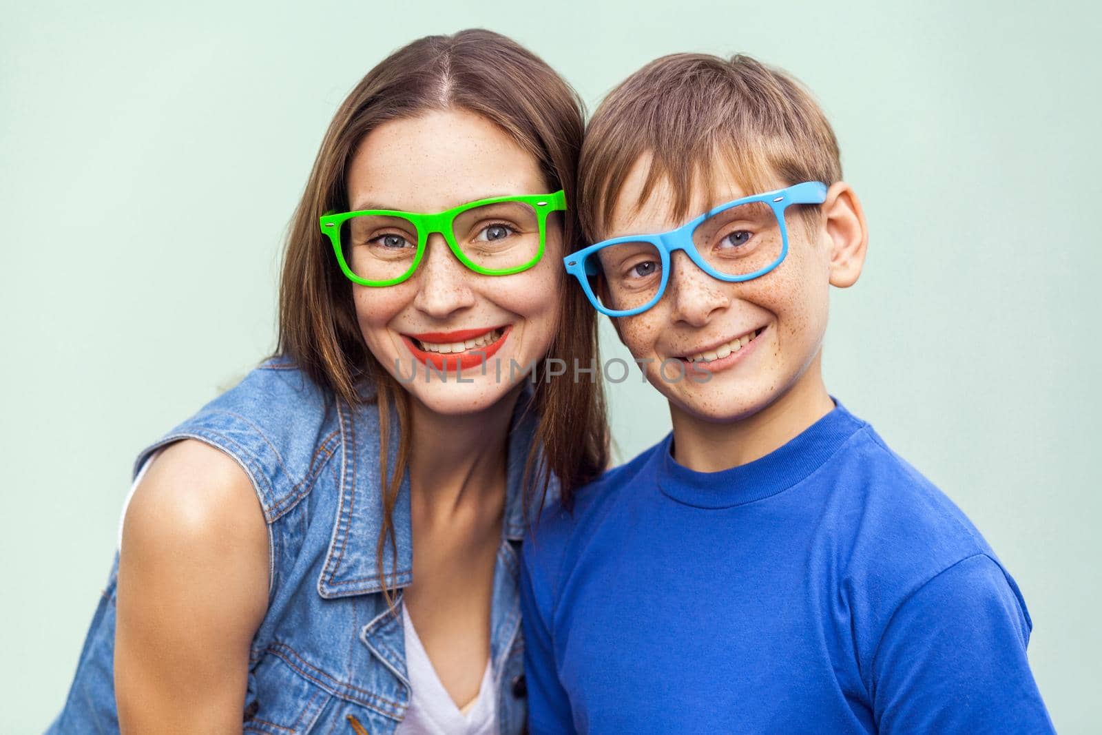 Eyewear concept. Hipster style. Portrait of gorgeous freckled brother and sister in casual t shirts wearing trendy glasses and posing over light blue background together. Studio shot