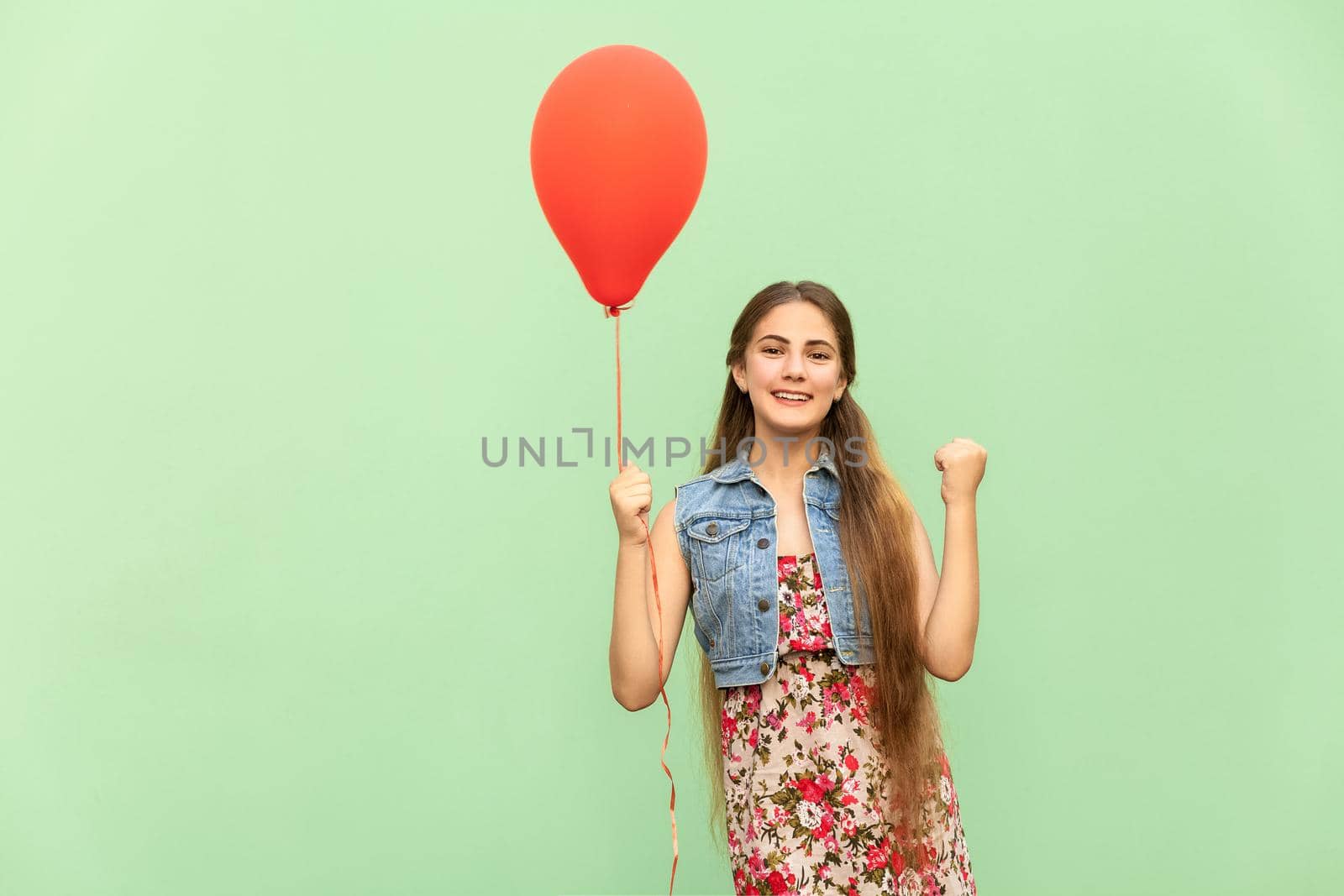 Its winn! The beautiful blonde teenager with red balloons on a green background. Isolated studio shot