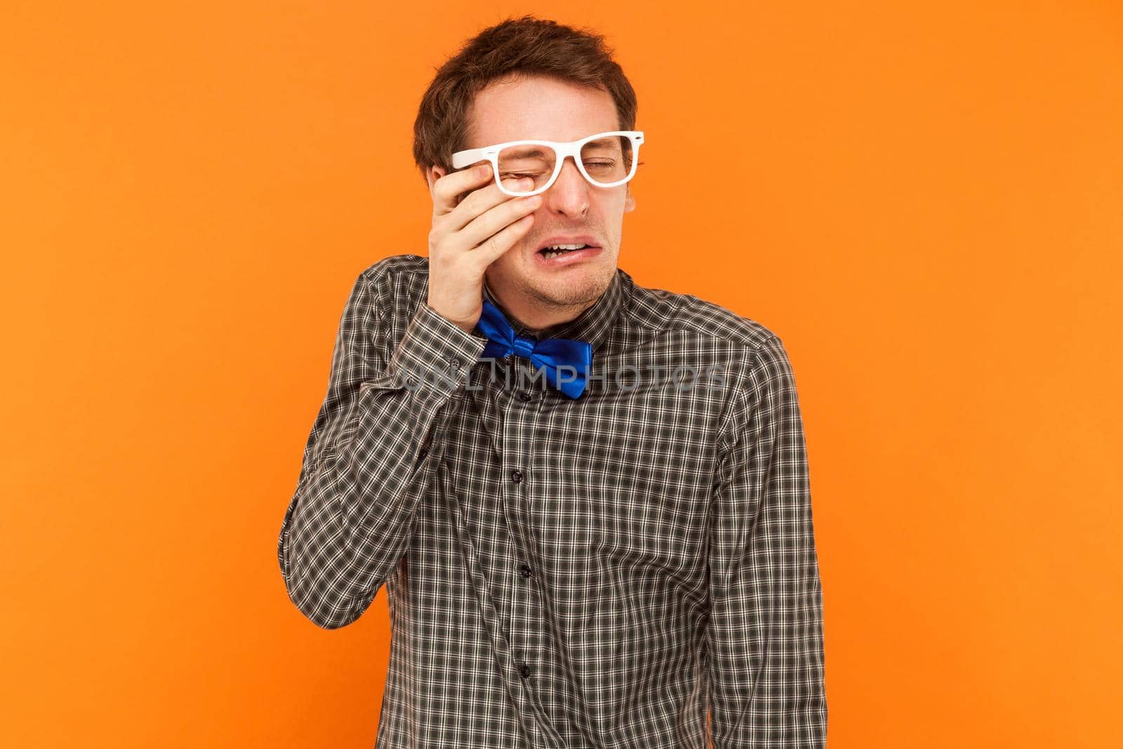 Emotional man crying and wipes away tears. Studio shot. Isolated on orange background