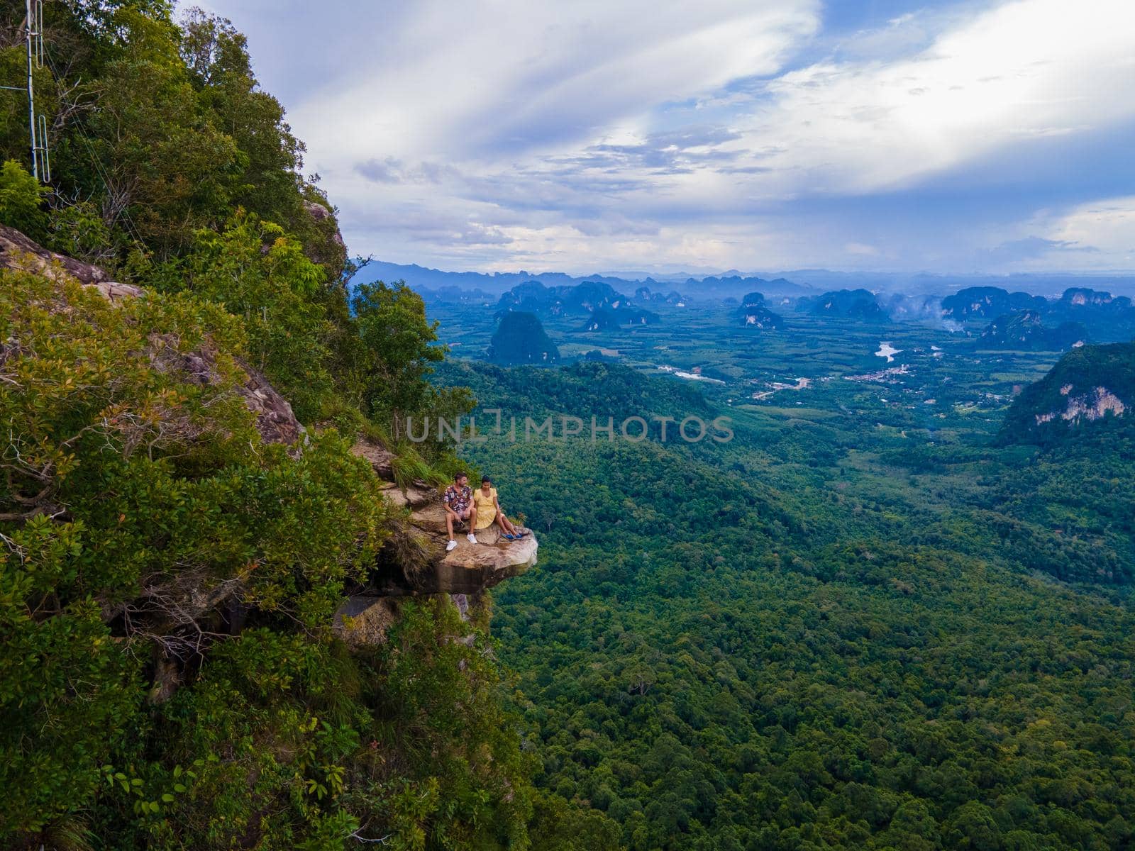 Dragon Crest mountain Krabi Thailand, a Young traveler sits on a rock that overhangs the abyss, with a beautiful landscape. Dragon Crest or Khuan Sai at Khao Ngon Nak Nature Trail in Krabi, Thailand