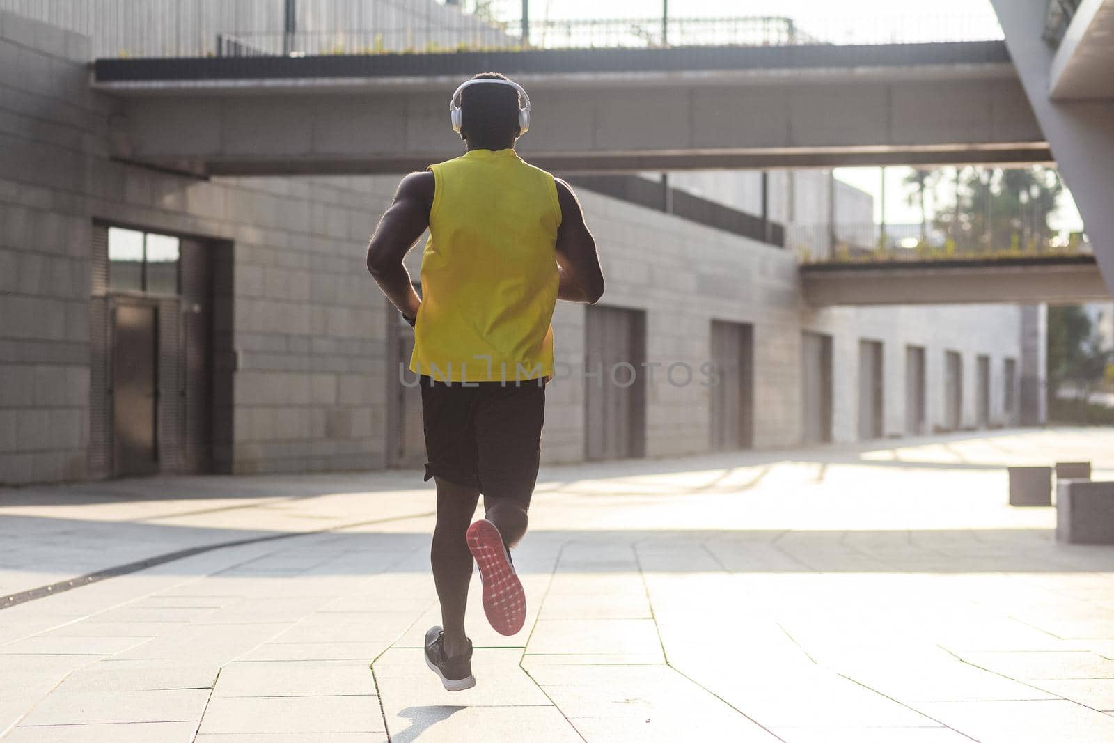 Young fit man in yellow t-shirt running sunset outdoors, autumn running, attractive dark skinned runner jogging fast in the park with beautiful light on background, sport concept