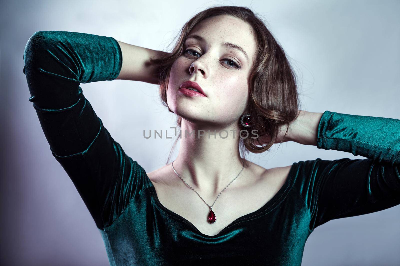 Portrait of beautiful woman with makeup, hairstyle and natural freckles on her face in green dress posing and looking at camera on gray silver background.