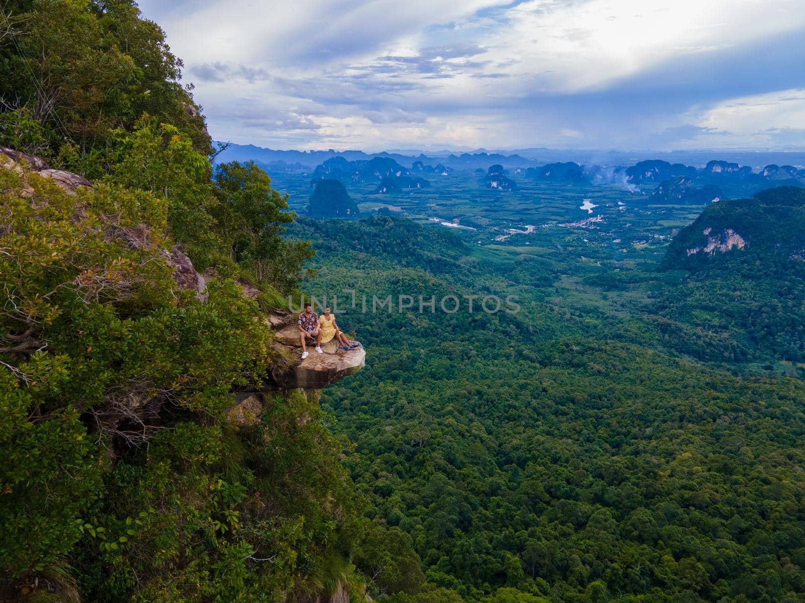 Dragon Crest mountain Krabi Thailand, a Young traveler sits on a rock that overhangs the abyss, with a beautiful landscape. Dragon Crest or Khuan Sai at Khao Ngon Nak Nature Trail in Krabi, Thailand