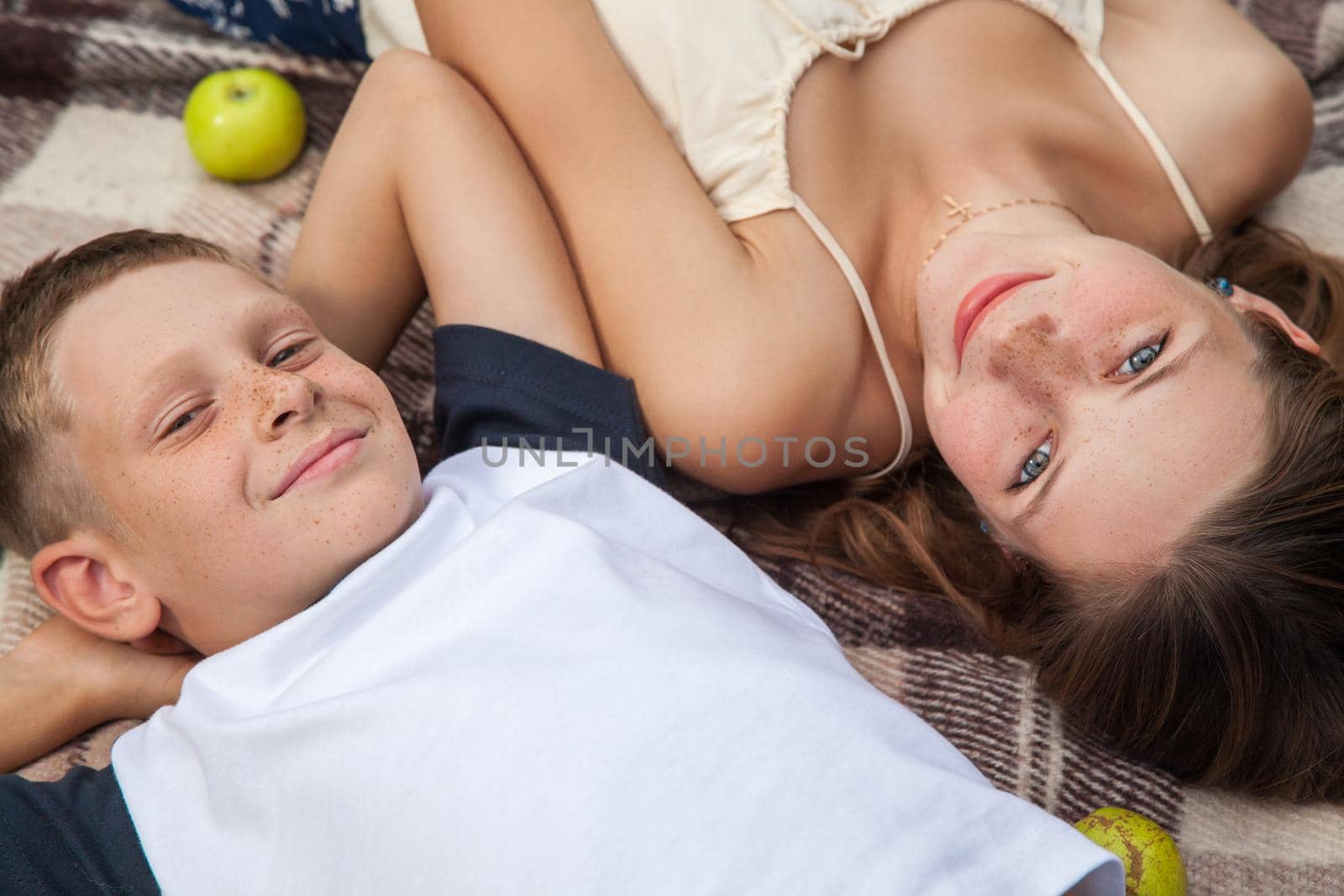 Happy young beautiful sister and brother with freckles on their faces posing lying down on plaid and smiling and looking at camera.