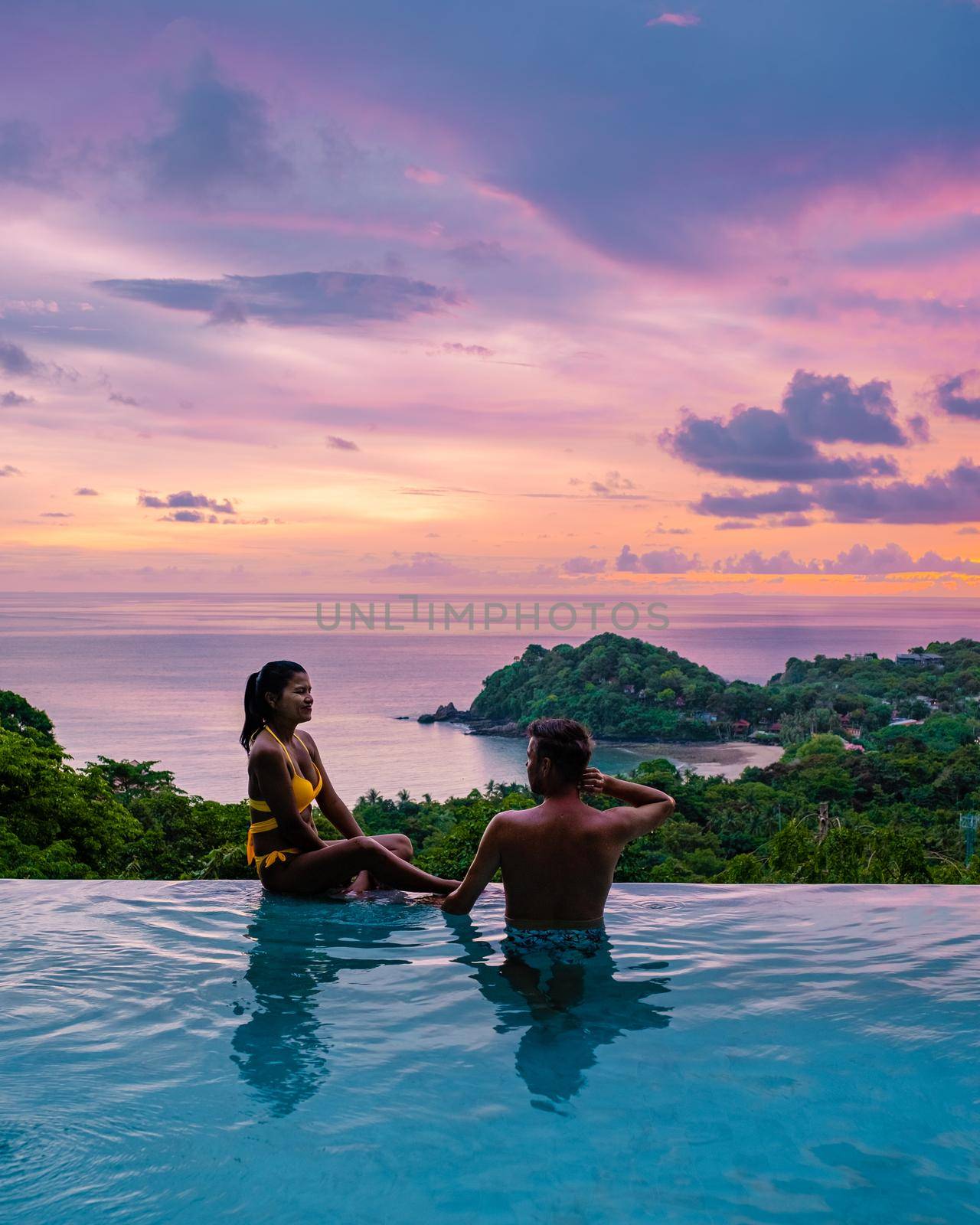 a young couple of men and women at a swimming pool during a vacation on a tropical island. man and woman in infinity pool during sunset. luxury vacation in Thailand pool of a luxury pool villa