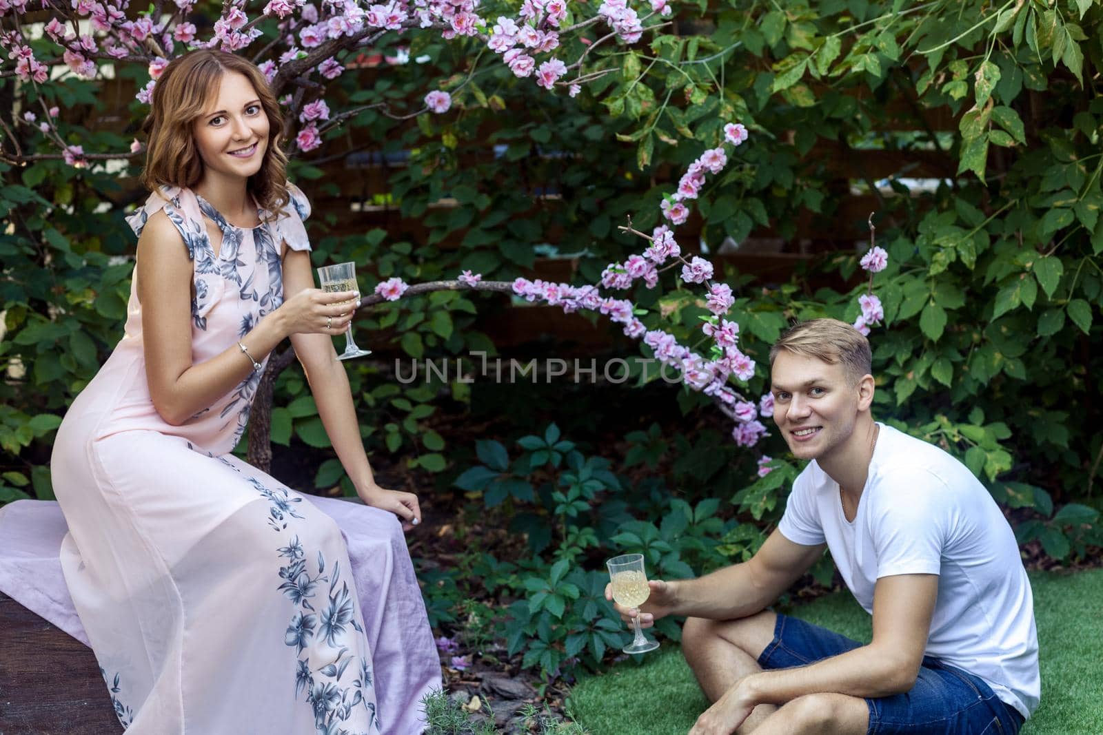 Young adult man says a toast. Holding Champagne glass, toothy smiling. Outdoor shot, spring park or summer concept. Love, sensual people