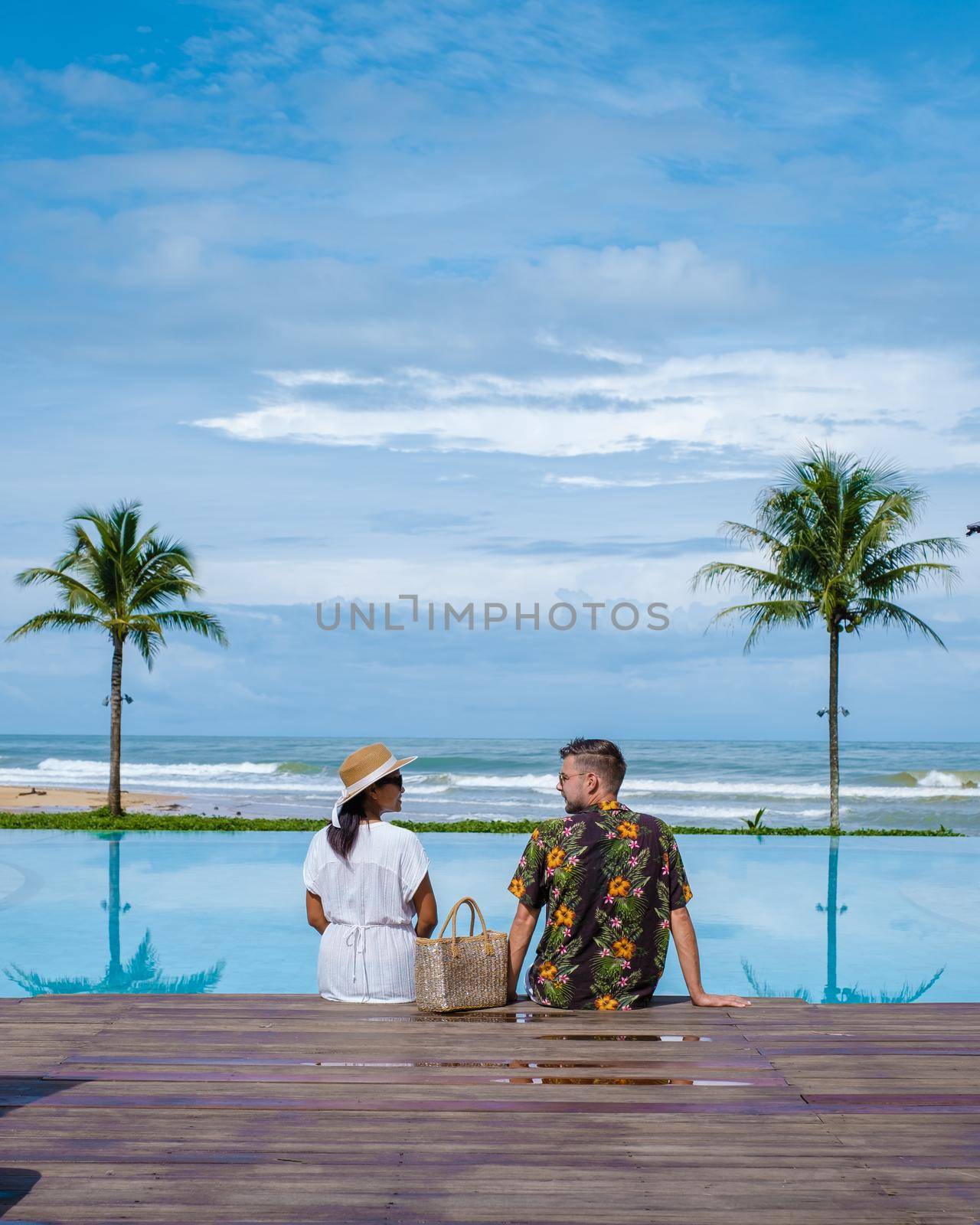 a young couple of men and women at a swimming pool during a vacation on a tropical island. man and woman in infinity pool during sunset. luxury vacation in Thailand pool of a luxury pool villa