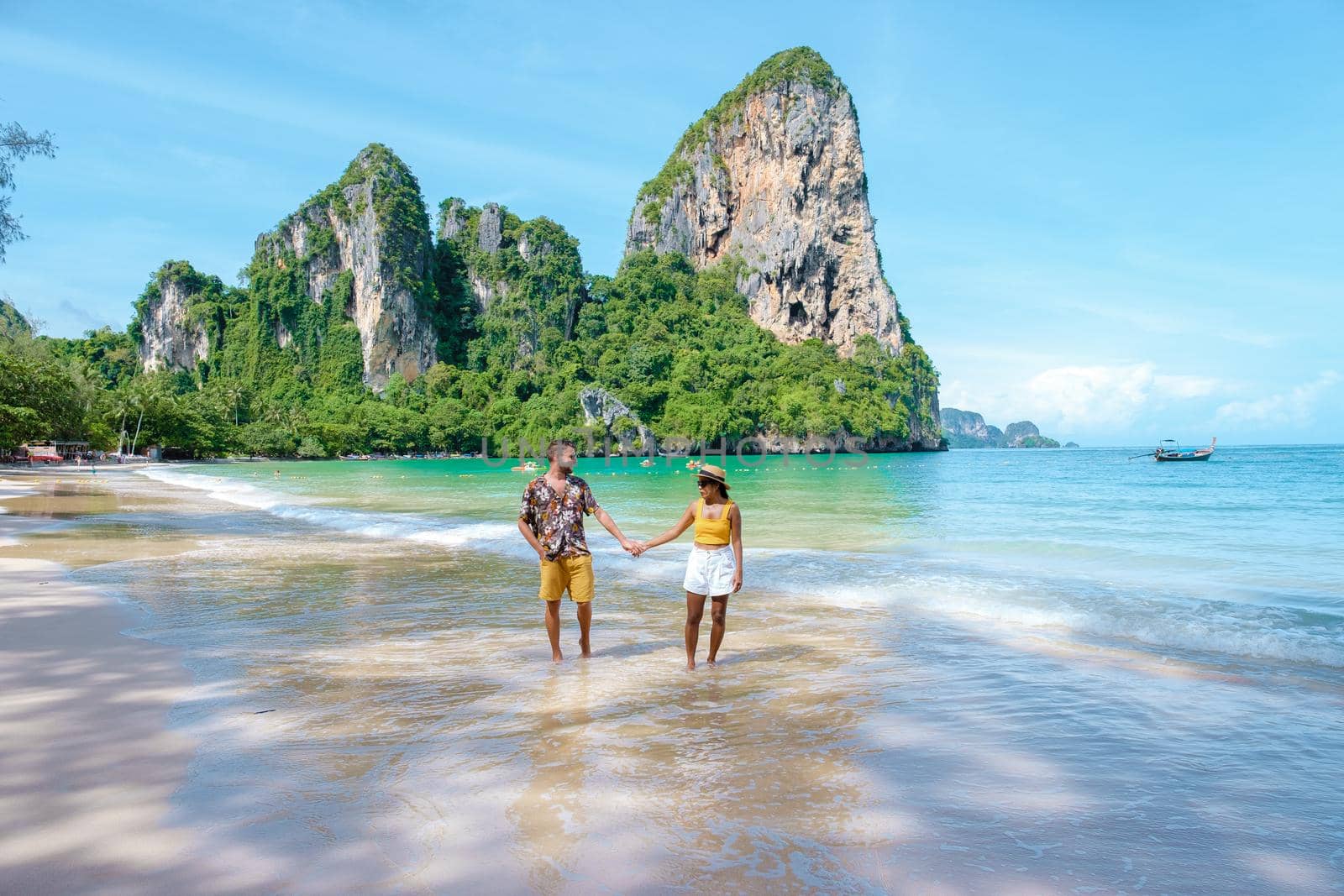 Railay Beach Krabi Thailand, the tropical beach of Railay Krabi, a couple of men and woman on the beach, Panoramic view of idyllic Railay Beach in Thailand with a traditional long boat.