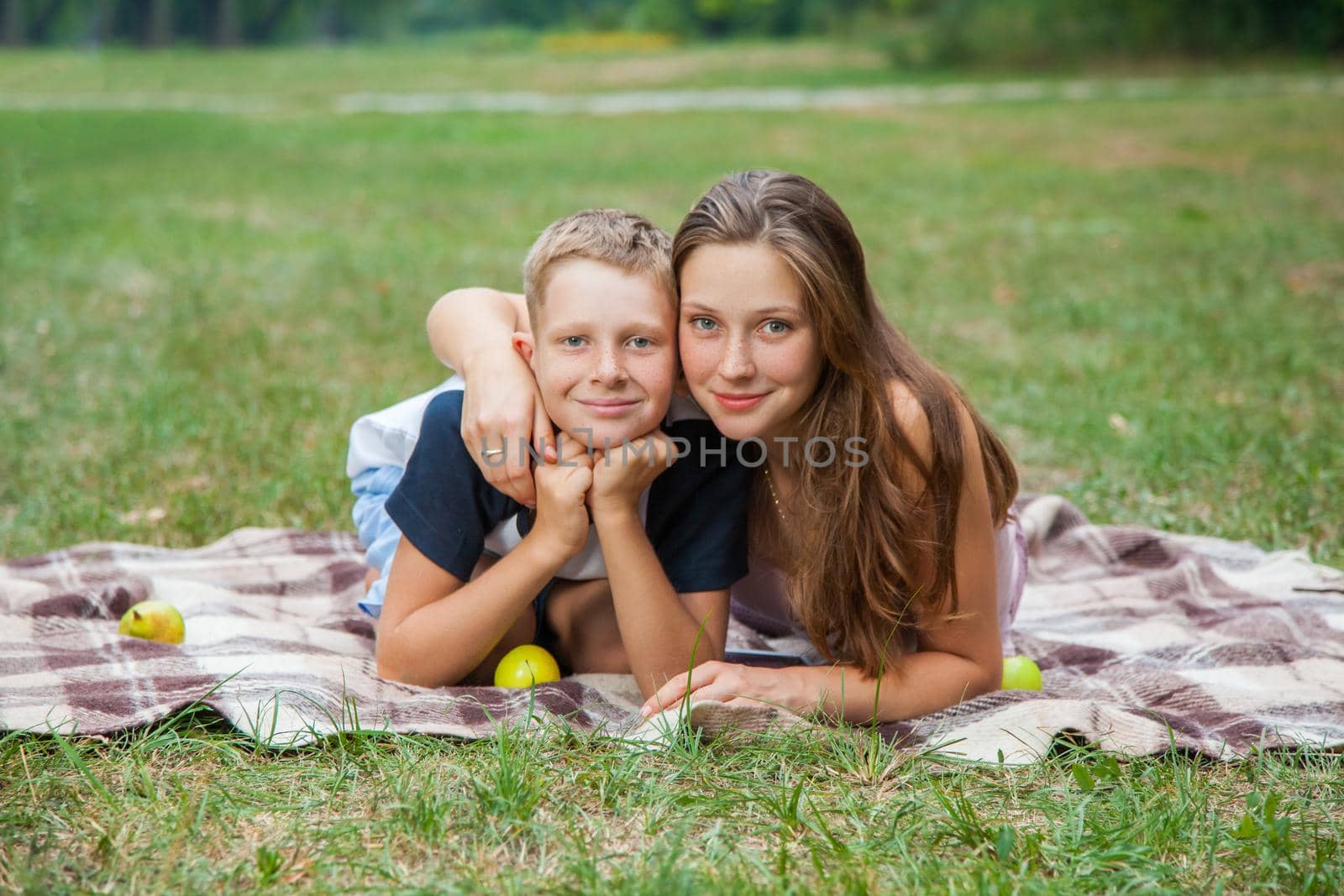 young beautiful brother and sister resting in the garden, looking and camera with smile. picnic summer time. lie down, top view.