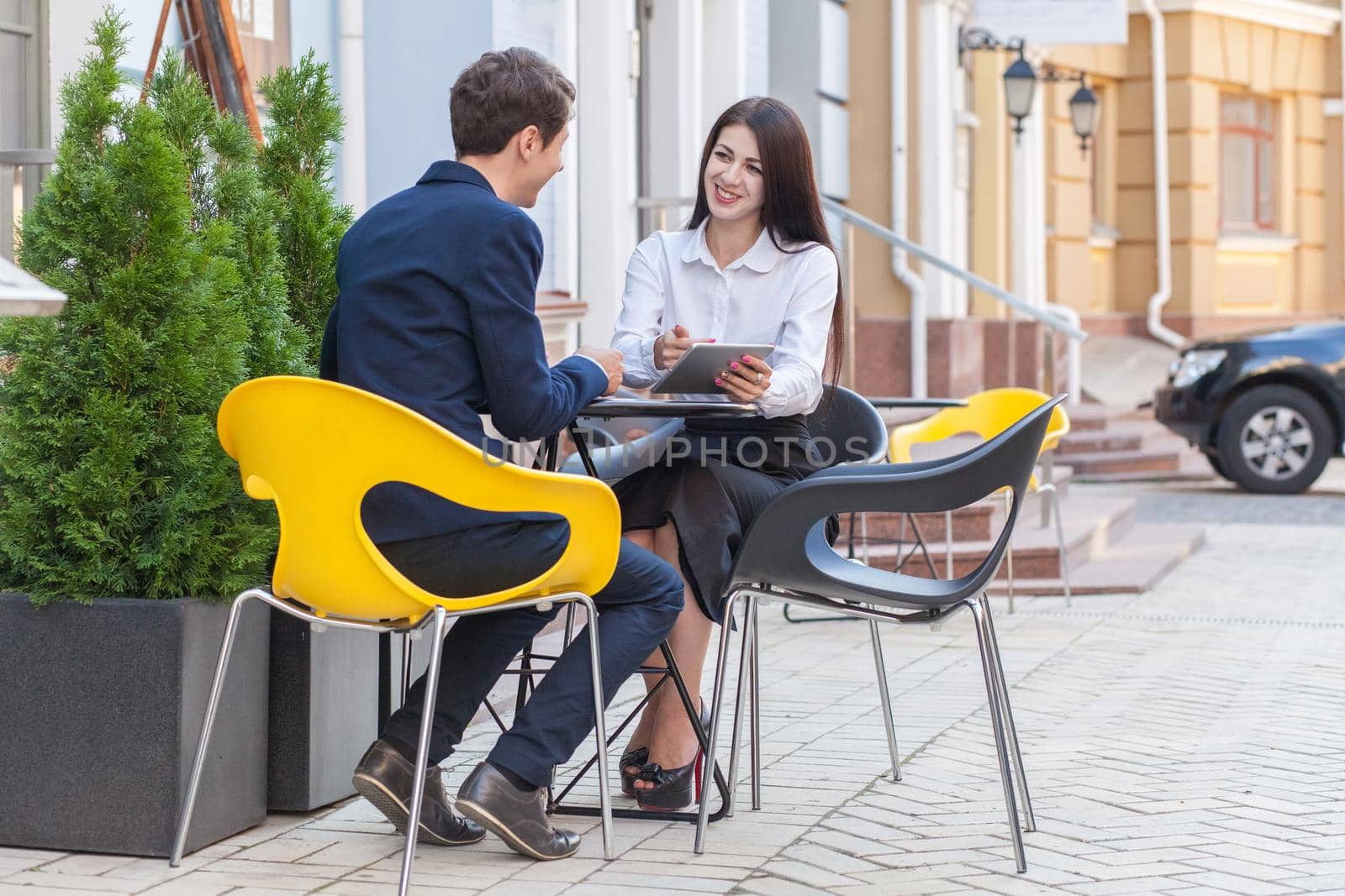 Two friends sitting outdoor in cafe thinking, looking at tablet and discussing their business.