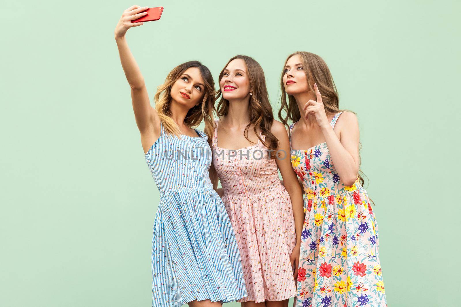 Young adult model, macking selfie, looking in smart phone screen and smiling. Isolated on green background. Studio shot