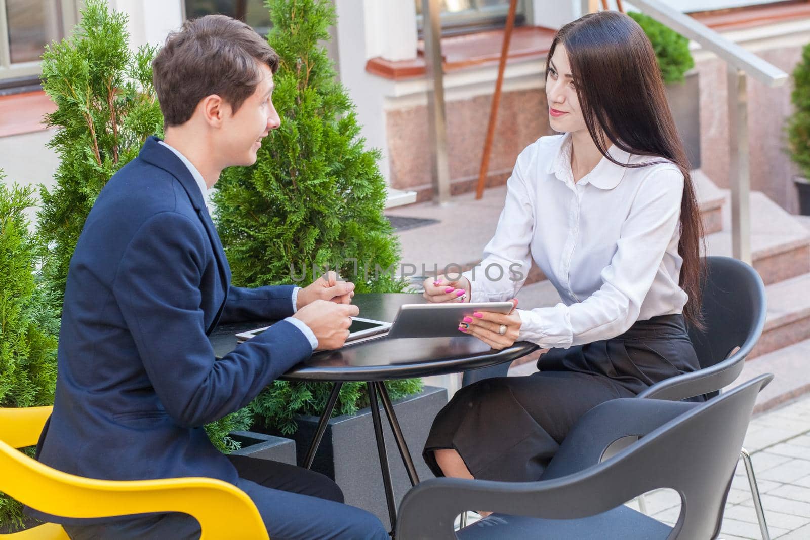 Two friends sitting outdoor in cafe thinking, looking at tablet and discussing their business.