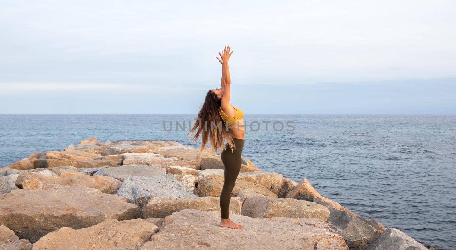 Panoramic image of young woman doing yoga on a breakwater near the sea. Urdva hastasana pose. Copy space. Healthy and active lifestyle.