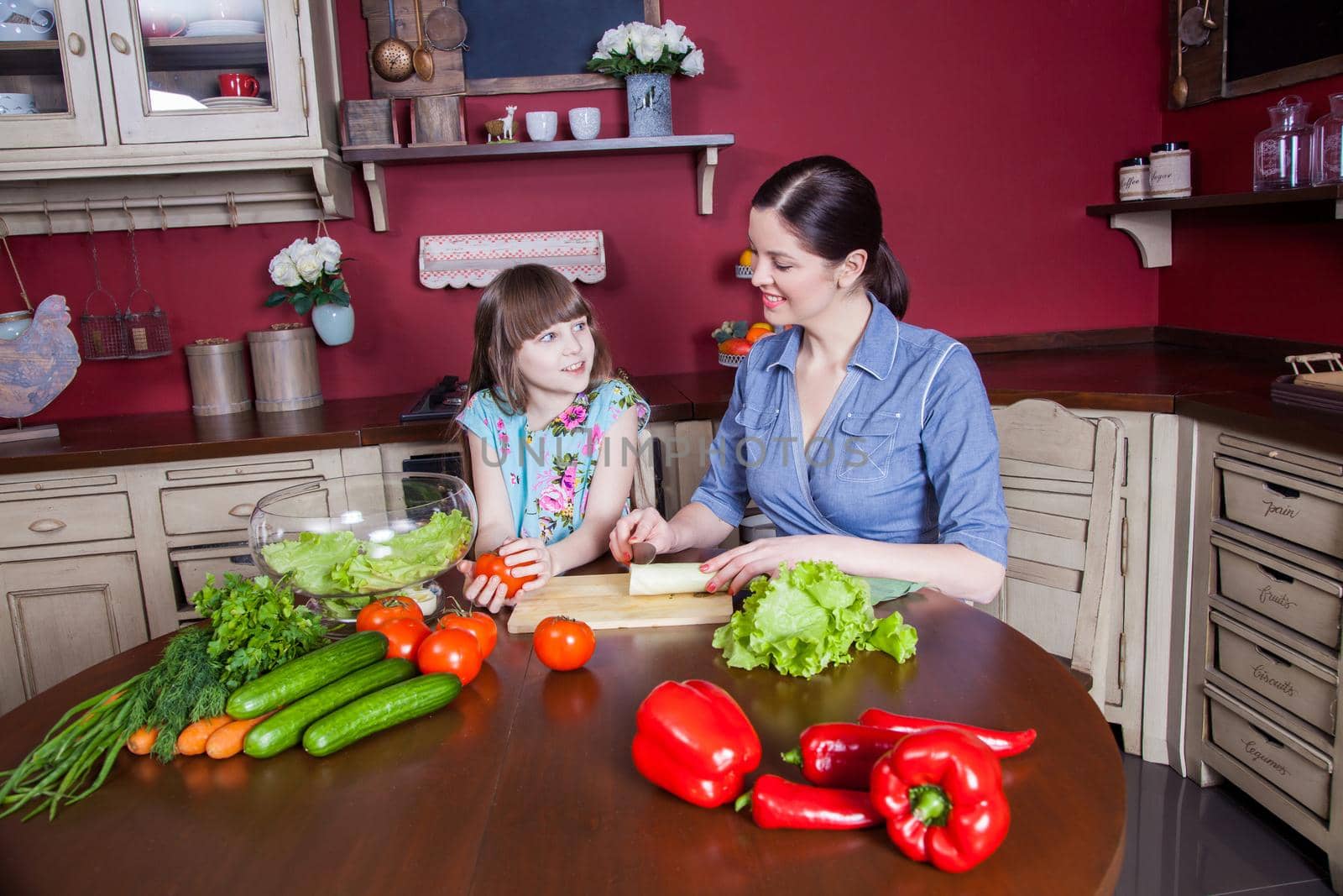 Happy mother and daughter enjoy making and having healthy meal together at their kitchen. they are making vegetable salad and having fun together. mom take care of her daughter and tech how to cook.