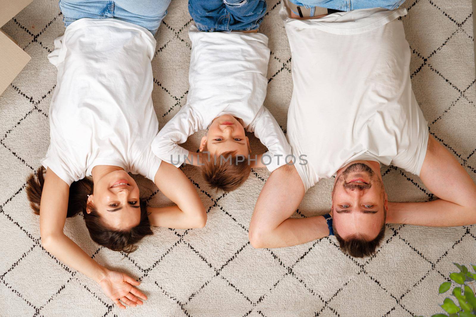 Happy family lying on the floor in new home with cordboard boxes around by Fabrikasimf