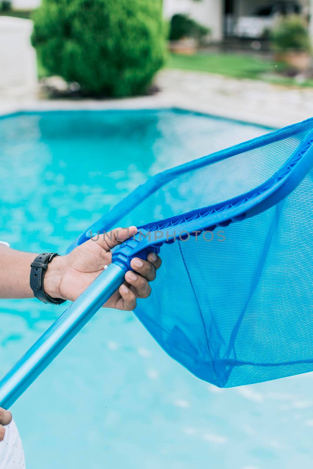 Hands holding a skimmer with blue pool in the background, A man cleaning pool with leaf skimmer. Man cleaning the pool with the Skimmer, Person with skimmer cleaning pool