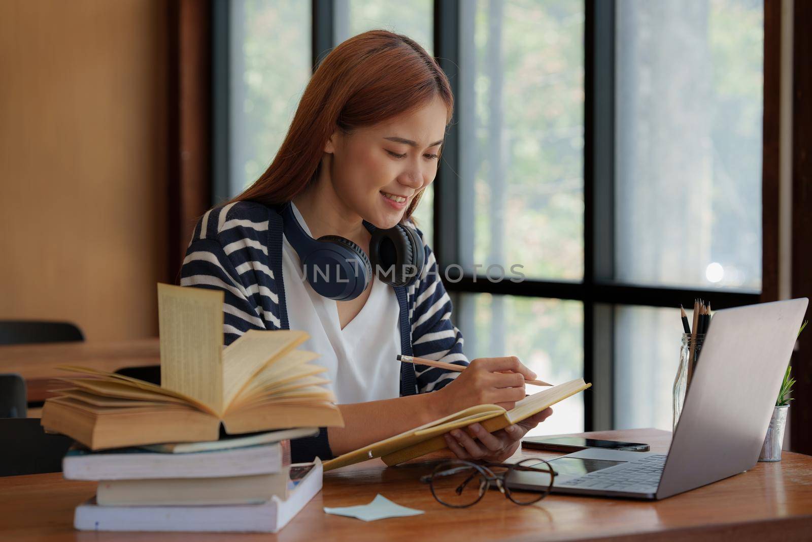 Young asian girl student wear headphone and writing a notebook and watching online class by laptop. e-learning education concept. by itchaznong