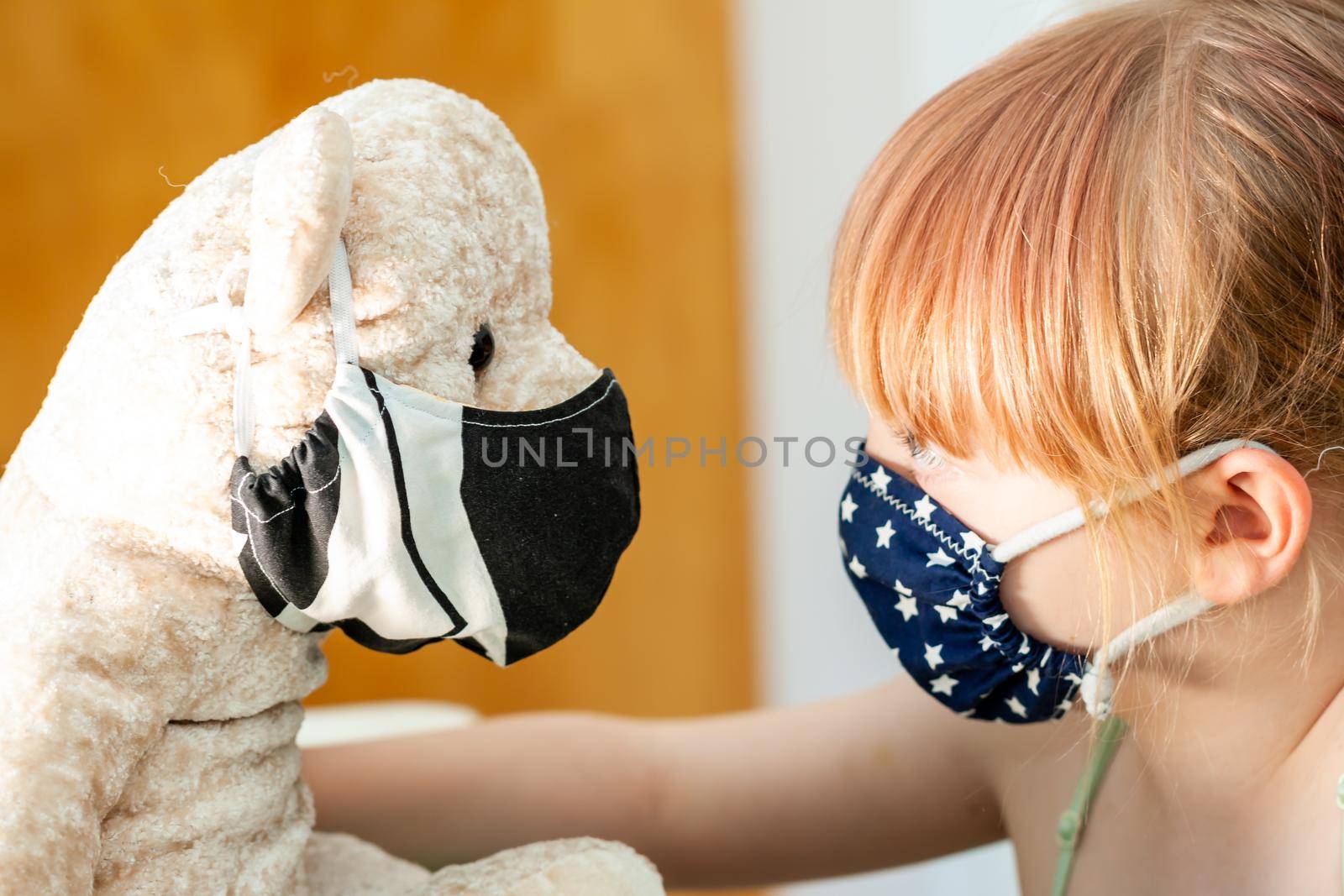 Young girl training to use a face mask during the pandemic -Focus on the teddy.