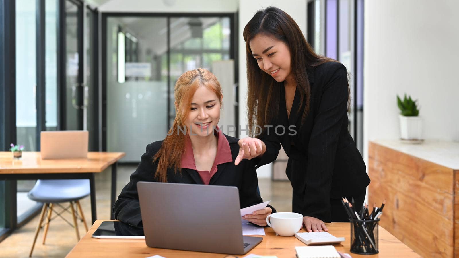 Asian female manager helping, giving advices to young intern at cooperate office by prathanchorruangsak