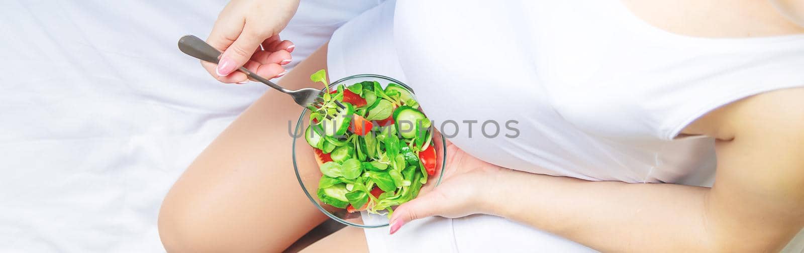 A pregnant woman eats a salad with vegetables. Selective focus. Food.