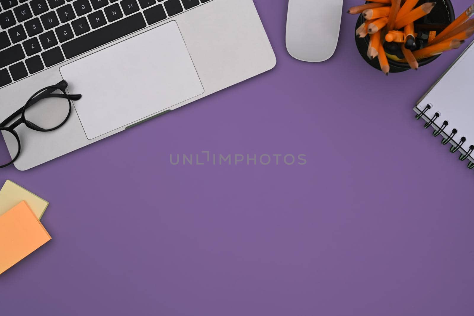 Stylish workplace with laptop computer, glasses, sticky note and notebook on purple background.