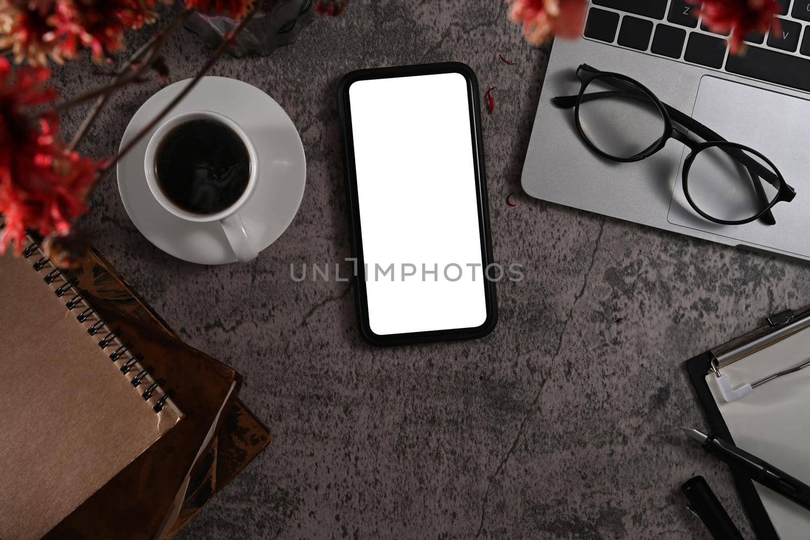 Above view smart phone with blank display, laptop, glasses, coffee cup and notebook on ark stone background by prathanchorruangsak