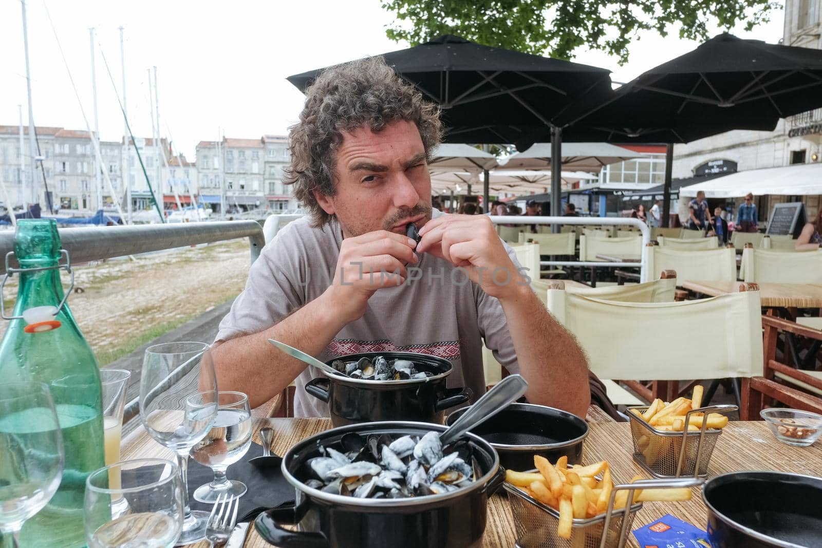Young man eatinYoung man eating mussels on a terrace of a French restaurant. Cloudy day, vacation mood